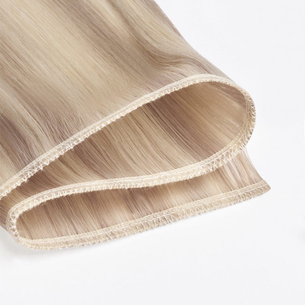 Products Extreme close-up of premium 100% virgin remy cuticle human hair machine weft extensions with reinforced double stitching in highlight blonde for B2B wholesalers and salons.